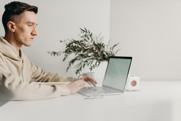 Jongeman zit aan tafel op laptop