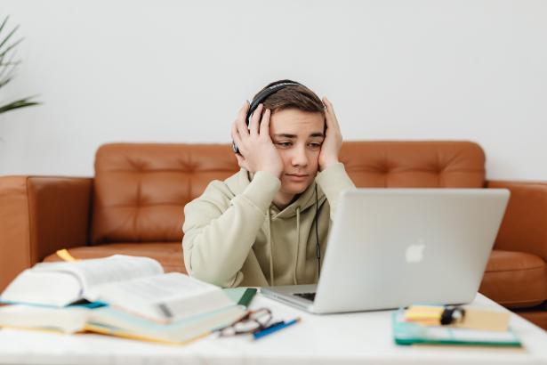 Jongen zit op de grond achter zijn laptop met zijn handen op zijn hoofd