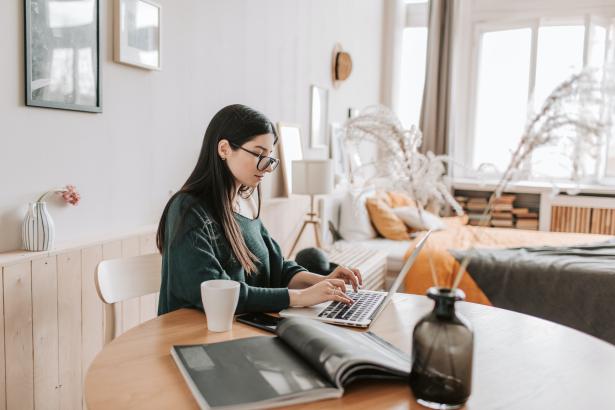 Vrouw met groen shirt en bril zit aan tafel op haar laptop 