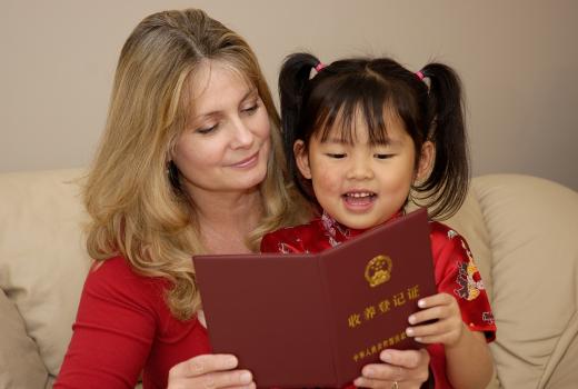 Blonde vrouw leest boek met peuter met Chinese uiterlijke kenmerken op schoot